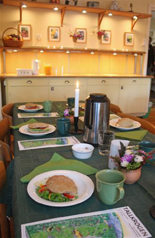 Dukat bord med smörgåsar, kaffe och blommor i en hemtrevlig miljö.