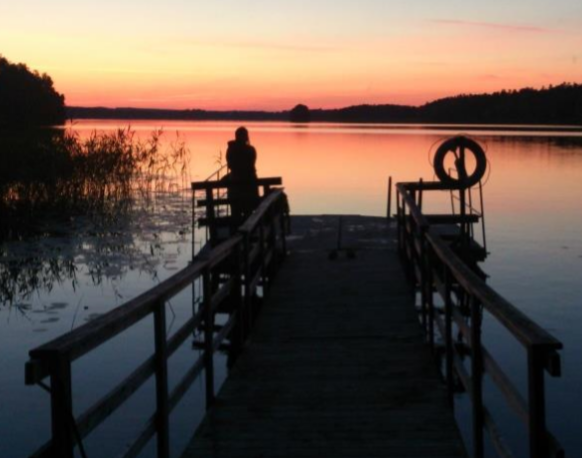 En person står på bryggan och ser ut över solnedgången över sjön.